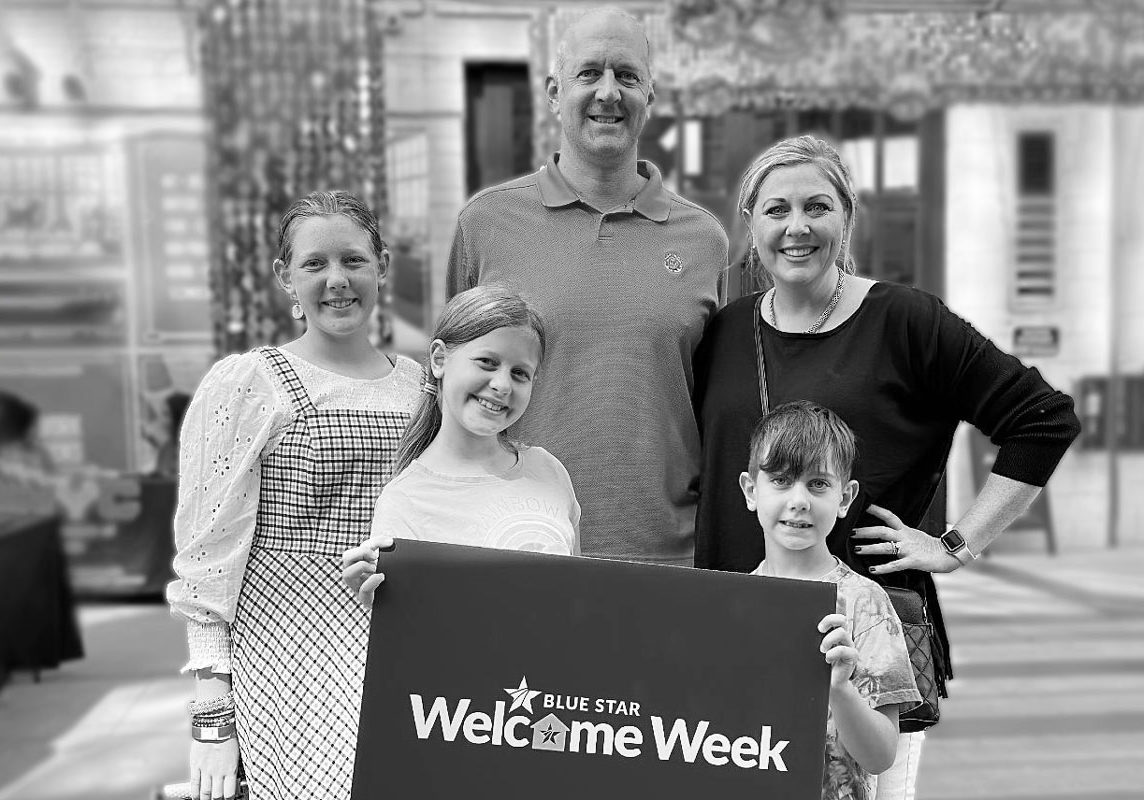 a husband, wife and 3 young children holding a Blue Star Families Welcome Week sign